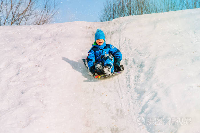 孩子们冬天好玩滑动在雪地里的小男孩