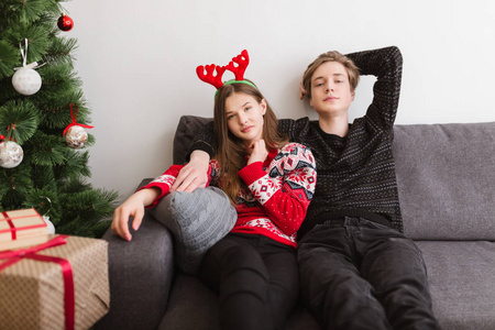 年轻美丽的情侣坐在沙发上的肖像在家里, 朦胧地看着相机与圣诞树附近