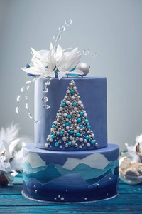 分层蛋糕的蓝色蛋糕与圣诞树和白色的花朵在上面的形象。节日甜点的概念