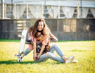 两个年轻的混血女孩在休闲服装与滑板摆在绿色草坪上