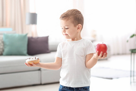 小男孩与甜甜的甜甜圈和新鲜的苹果在房间里