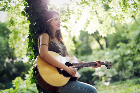 美丽的女人玩声学吉他，在自然