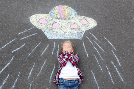 小女孩躺在粉笔画外星宇宙飞船上的柏油