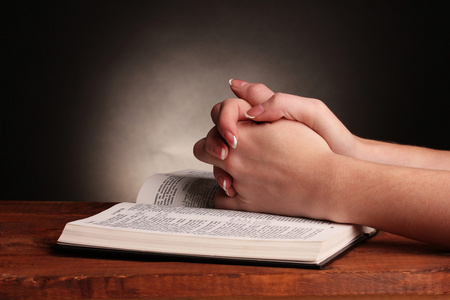 手折在祷告中打开俄罗斯神圣的圣经黑色背景上照片