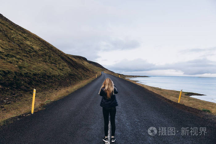 在寒冷的雨天站在路边欣赏风景的年轻女子观