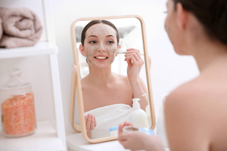 妇女在镜子前面应用擦洗在面孔在家