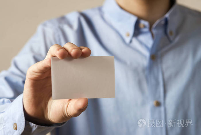 在混凝土墙体背景下手持白色卡片的休闲男子手合上