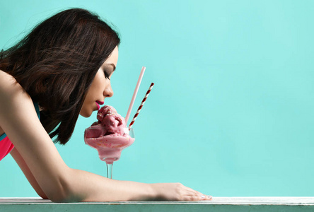 粉红色帽子的年轻妇女吃草莓冰淇淋甜点在现代浅蓝色
