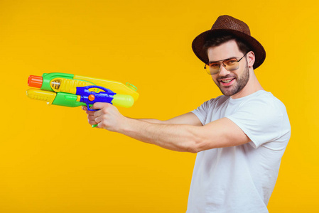 时尚的年轻人拿着水枪, 微笑着在黄色的相机隔离照片
