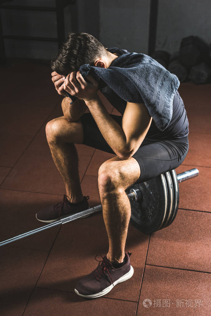 沮丧年轻运动员用毛巾在手坐在杠铃在健身房照片-正版商用图片03vsdy-