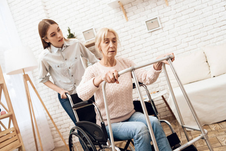 女孩护理老年妇女, 而她试图站起来, 从轮椅上的帮助沃克