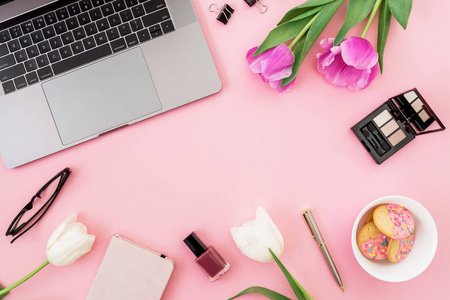 最热门的笔记本电脑周围的新鲜郁金香和化妆品在粉红色背景下的产品