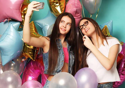 两个十几岁的女孩的朋友 colorfoul 气球使自拍的电话。蓝色背景