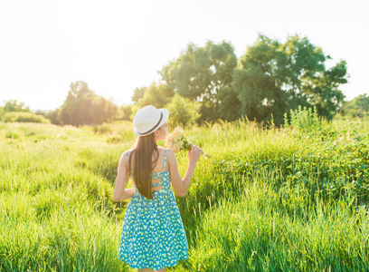 年轻的黑发少女在绿地里, 可爱的女性在草地上轻松地穿着花裙.