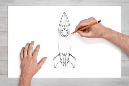 男性手用铅笔画一个圆形照明灯的太空火箭