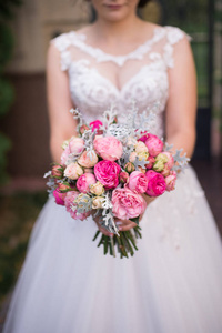 新娘手捧着粉红色玫瑰的婚礼花束。婚礼花束