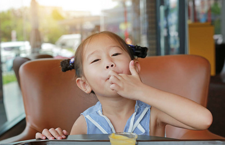 快乐的孩子的淡蓝色眼睛的小孩吃手指抬头灰色垃圾墙上的年轻成年妇女
