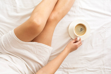 柔软的女人在床上的照片与一杯咖啡。顶部视图