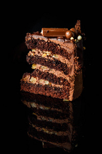 一块美味的巧克力蛋糕与奶油间层装饰巧克力糖果服务于黑色镜子背景
