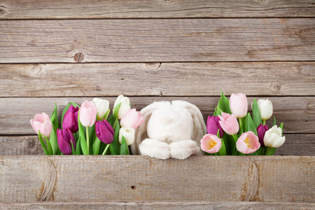 五颜六色的郁金香花束和兔子玩具在木墙壁前面。复活节贺卡。带空格的文本