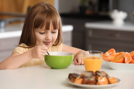 有趣的小女孩在家里吃早饭和喝柑橘汁