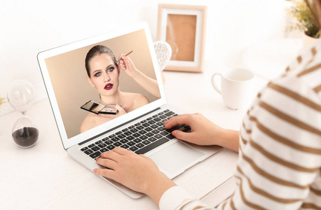 妇女观看在线培训专业化妆艺术家在笔记本电脑在桌上
