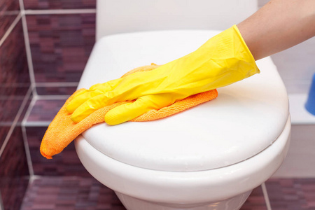 妇女用黄色橡胶手套清洁马桶座盖与橙色布。卫生间和卫生间卫生