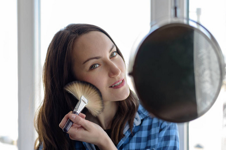 带化妆刷化妆镜的快乐女人应用于皮肤色调