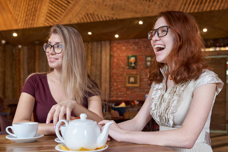 调情的年轻女友喝茶在一张桌子上, 热情快乐的面孔看着周围发生的事情