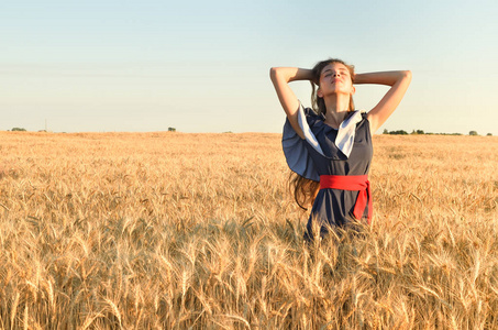 一个美丽的年轻女子把她的手放在田里的麦子上的山上