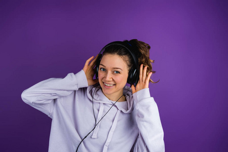 听音乐的美丽的女孩在紫色背景的运动衫上戴着耳机