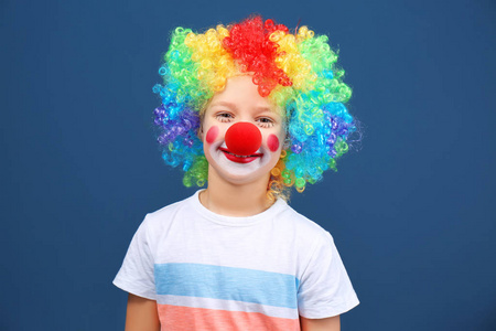 可爱的小男孩与小丑化妆在彩虹假发的颜色背景。愚人节庆典