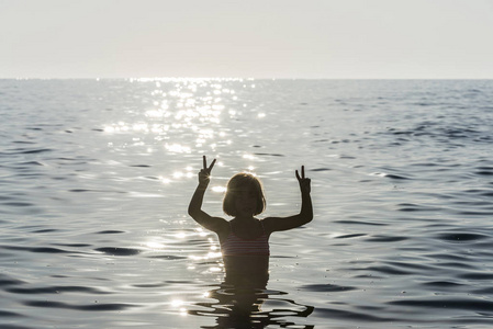 小女孩沐浴在海里做胜利的标志