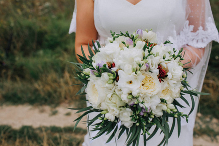 新娘穿一件衣服，站在绿色的花园和持有的鲜花和绿叶的婚礼花束