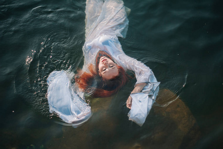 美丽的红头发的女孩漂浮在水中.洛基海岸.