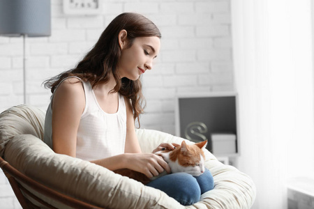 美丽的年轻女子与可爱的猫在扶手椅在家