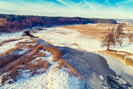 冬季下雪的乡村鸟瞰。结冰的河在雪的领域
