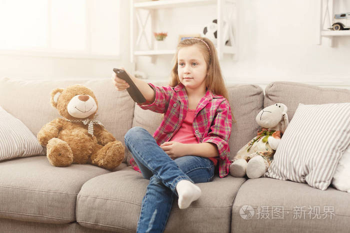 一个美丽的休闲小女孩坐在沙发上在家看电视