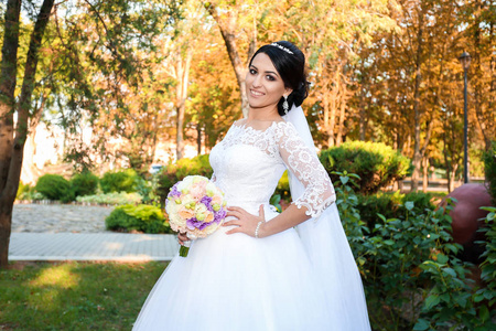 美丽的新娘在婚礼的日子在秋天森林的背景与一个美丽的花束