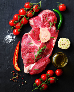 生肉, 牛排在一块石材切割板与迷迭香, 香料, 盐, 油, 樱桃西红柿, 辣椒和草药