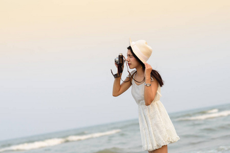 亚洲妇女戴着白色连衣裙的帽子在碧上拍照