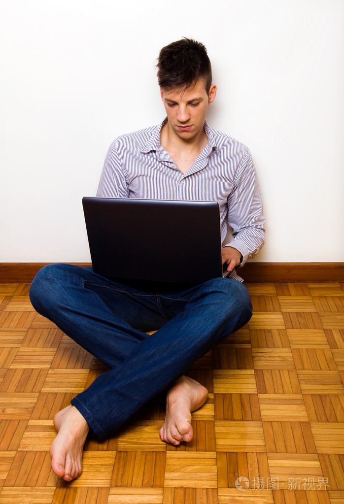 年轻男子坐在地上在红磡的便携式计算机上工作
