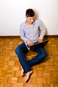 年轻男子坐在地上在红磡的便携式计算机上工作