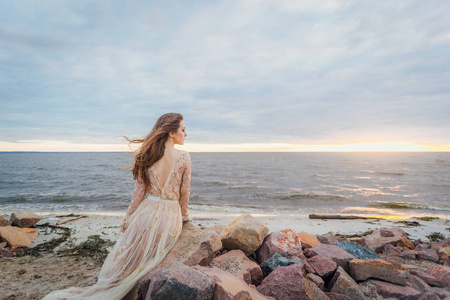 日落时分, 年轻漂亮女子在海边的婚纱礼服上摆造型
