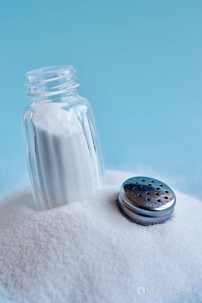 蓝色背景下洒盐和打开 saltshaker 的特写照片照片