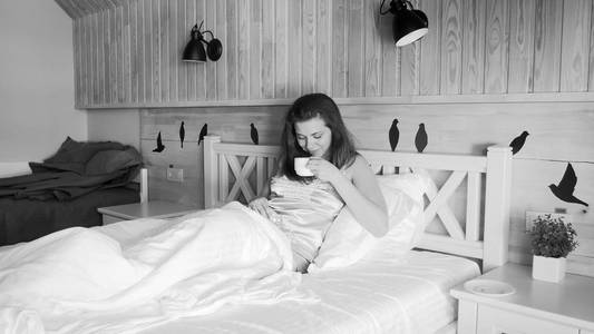 年轻女子清晨在床上喝咖啡的黑白图像