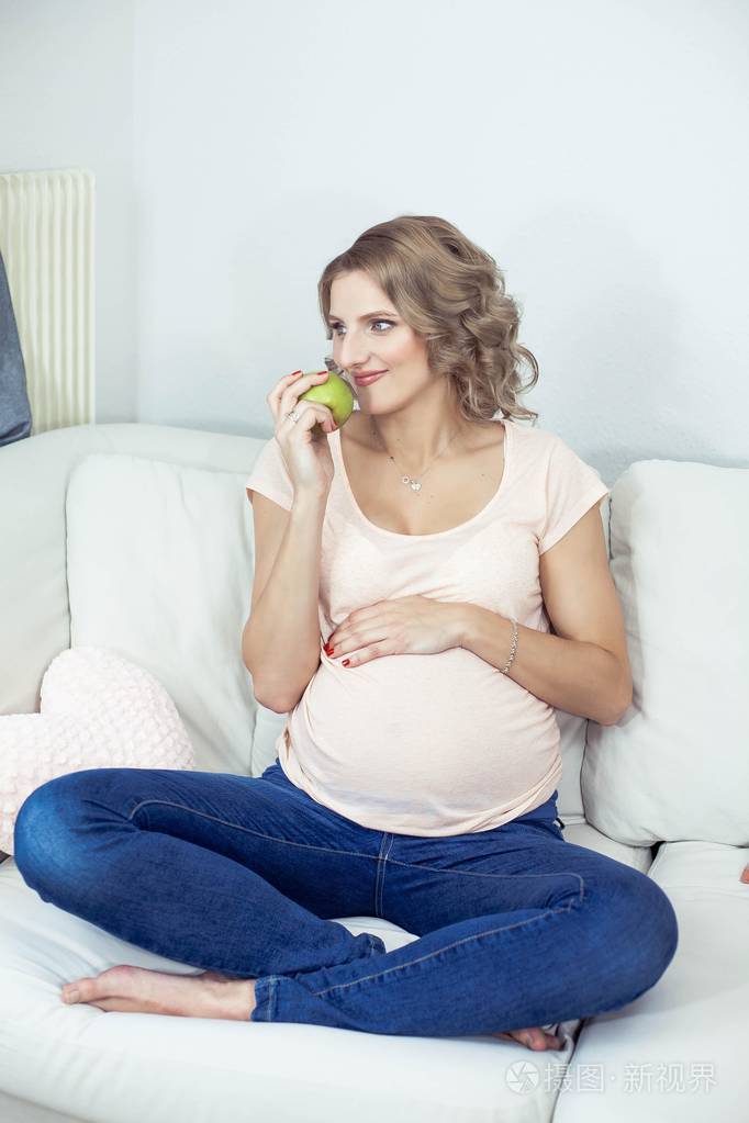 年轻漂亮的孕妇正在家里休息年轻的孕妇正在吃苹果健康一个美丽的孕妇
