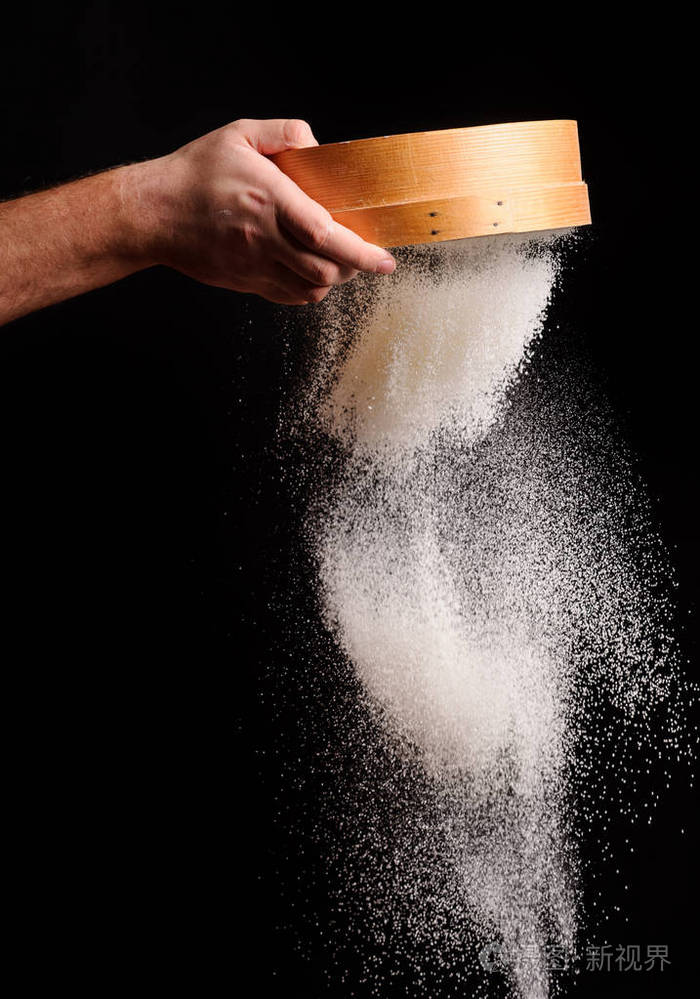 男人的手是通过筛上的黑色背景筛选面粉