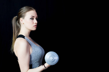 一个穿灰色便携形式的漂亮女孩举起沉重的灰色哑铃照片