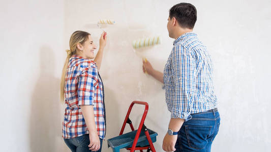 微笑的年轻夫妇在新房子里粉刷墙壁